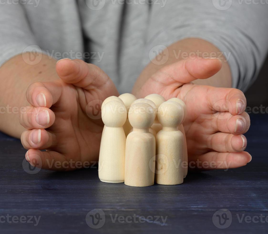 mãos femininas protegem figuras de madeira de homens. conceito de proteção e orientação. preservação da equipe em momentos de crise foto