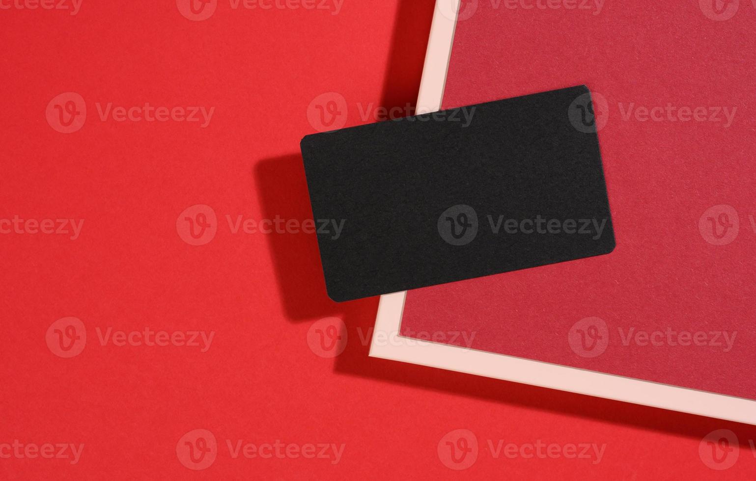 cartão de visita retangular preto em branco encontra-se em um fundo vermelho moderno com folhas de papel vermelhas com uma sombra. modelo de negócios foto