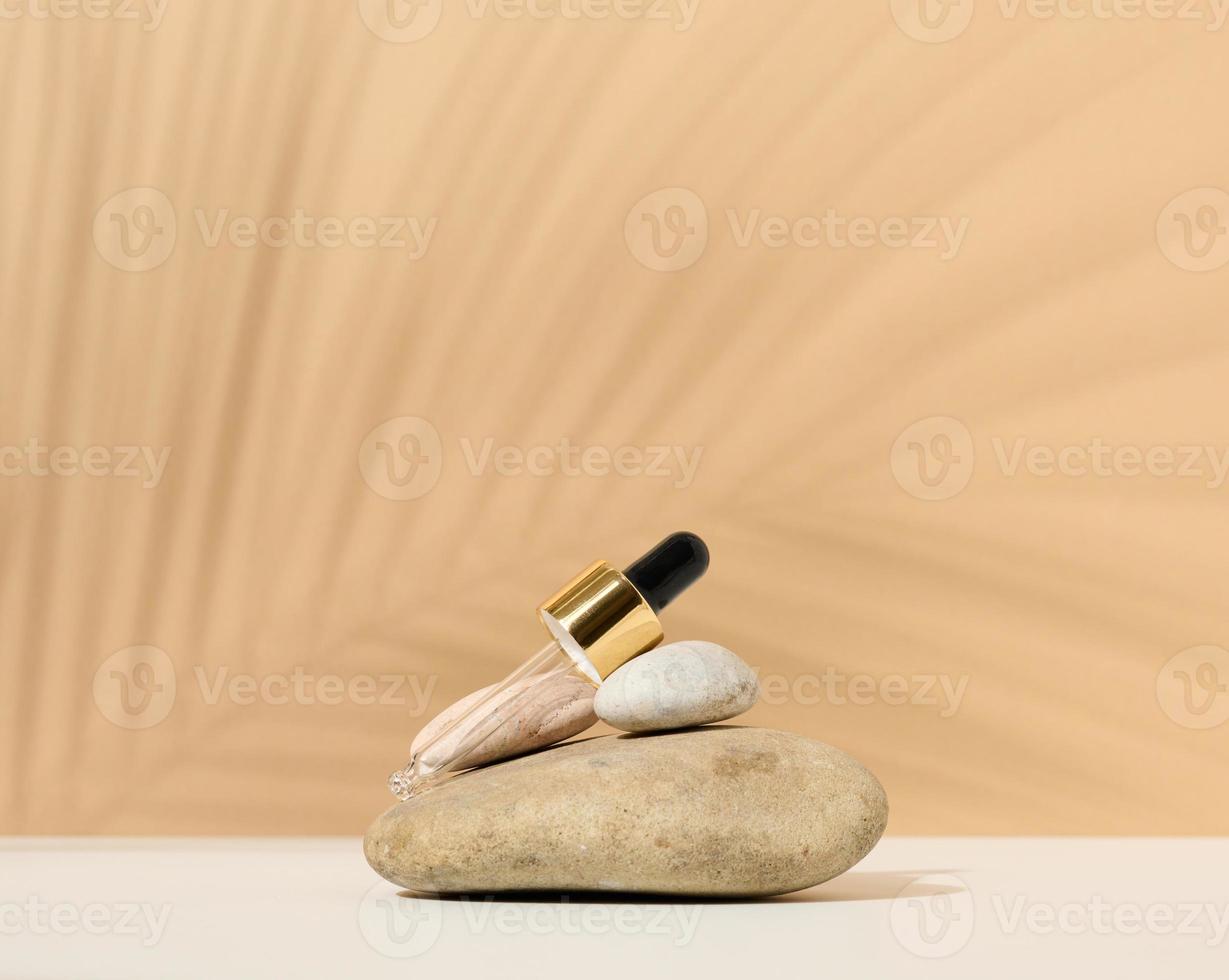 uma pipeta de vidro para um frasco cosmético está sobre uma pilha de pedras, a sombra de uma folha de palmeira foto