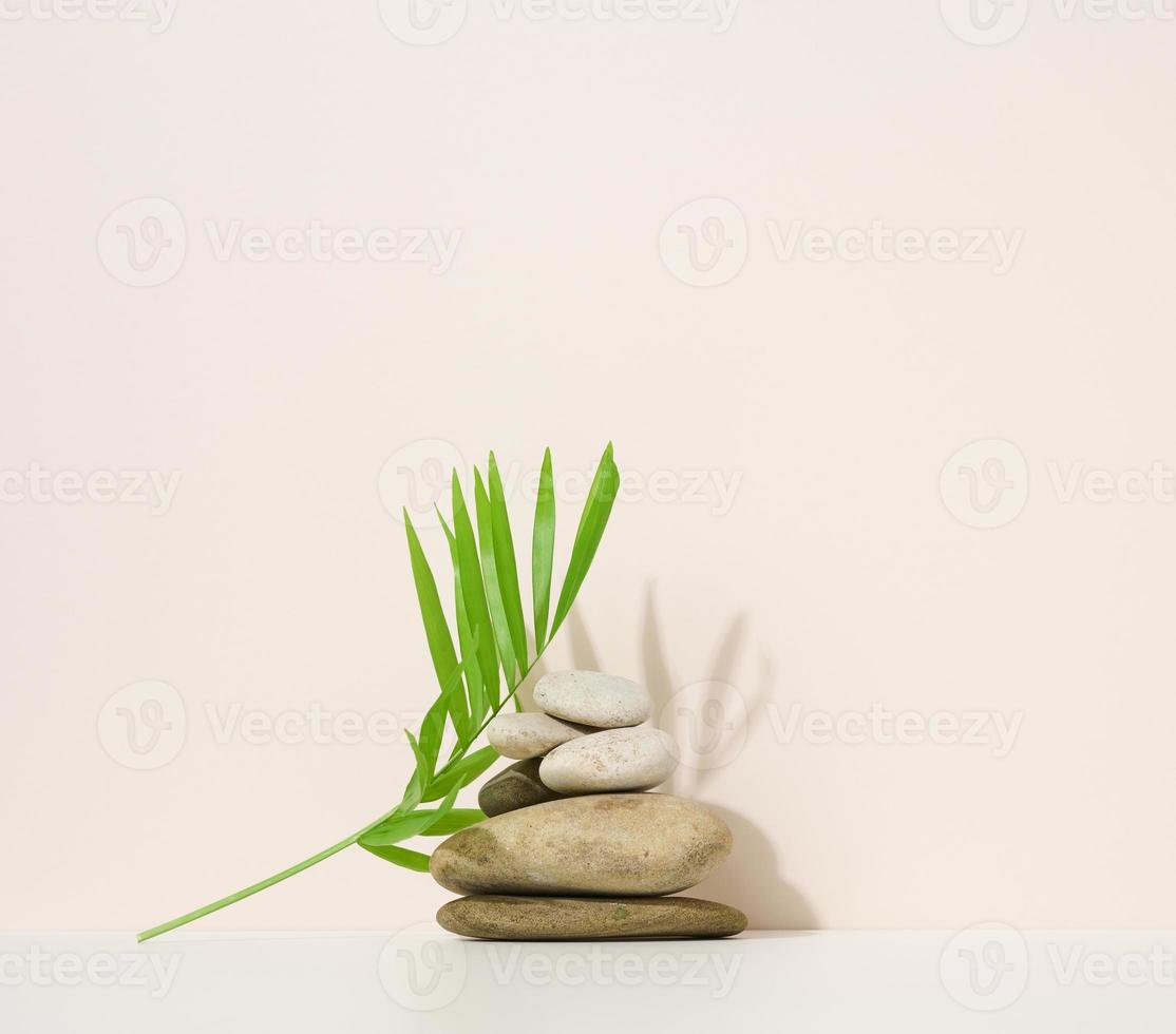 pilha de pedras redondas e folha de palmeira verde sobre um fundo bege. cena para demonstração de produto cosmético foto