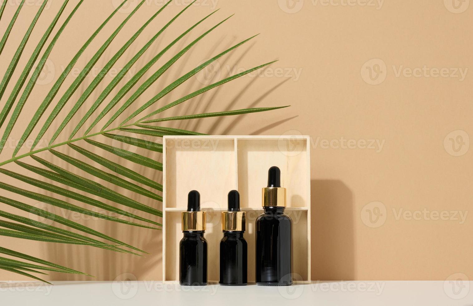 garrafa de vidro marrom com pipeta sobre fundo marrom claro, perto de folha de palmeira. maquete de produto cosmético para cuidados com a pele foto