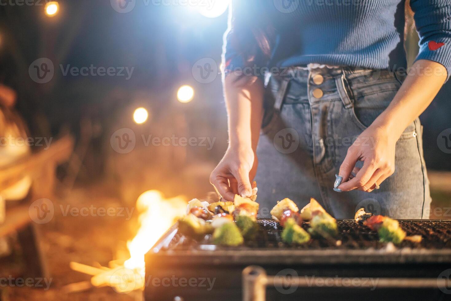 feche a mão da mulher cozinhar carne na churrasqueira na festa de ano novo. bar-bq ou churrasco no fogão tradicional. festa noturna, pessoas e conceito de celebração. foto