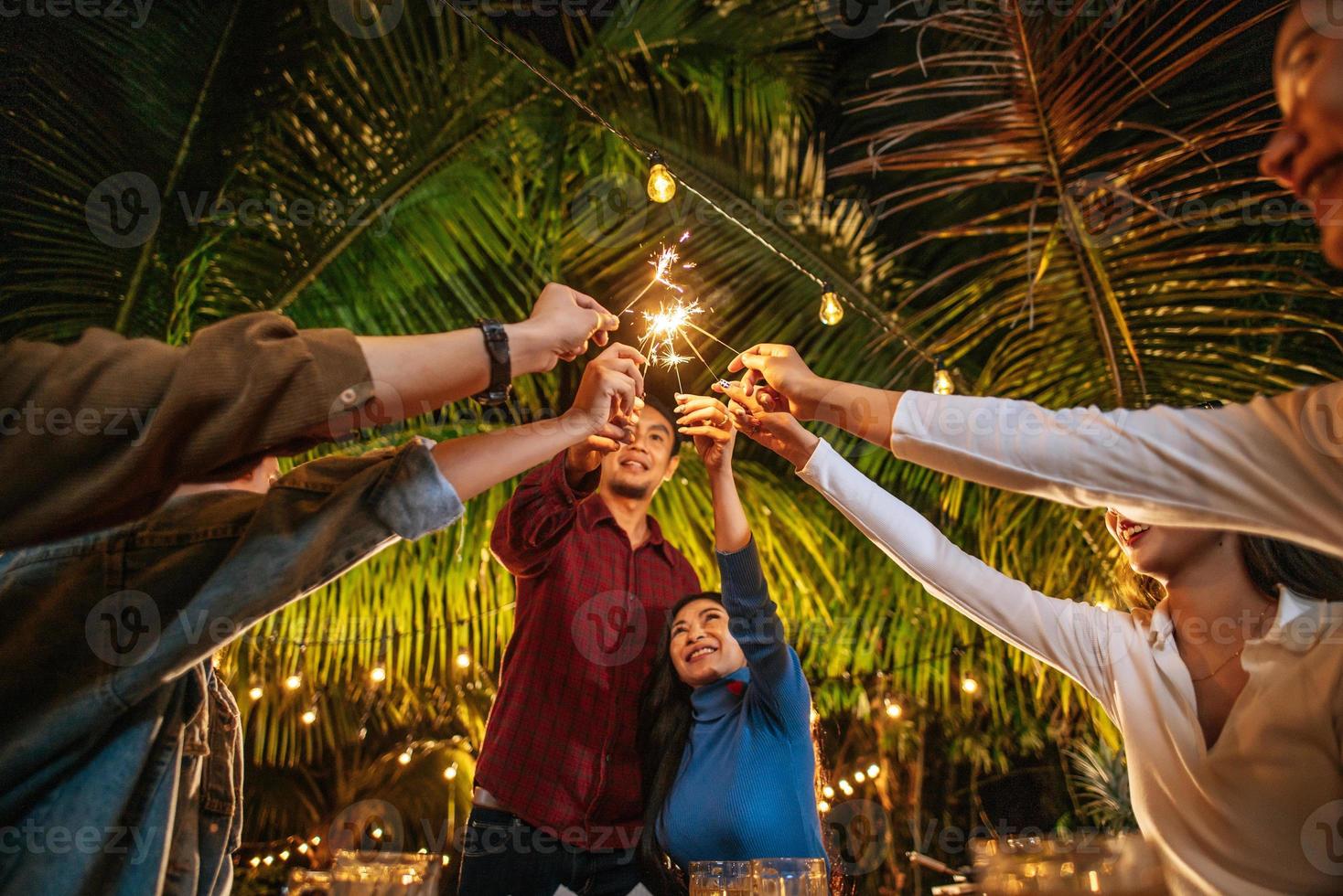 retrato de feliz grupo asiático de amigos se divertindo com estrelinhas ao ar livre - jovens se divertindo com fogos de artifício durante a noite - pessoas, comida, estilo de vida de bebida, conceito de celebração de ano novo. foto