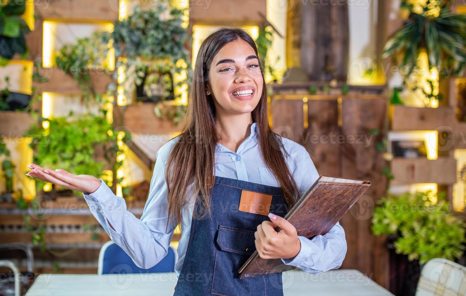 feliz linda garçonete sorridente vestindo avental dando um menu de pasta em um restaurante, olhando para a câmera, em pé no café aconchegante, bom serviço foto