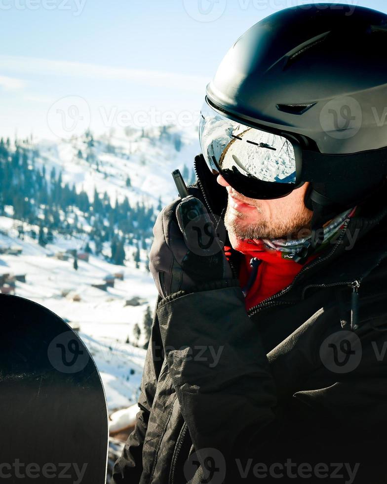 homem em equipamento de esqui, usando óculos de segurança, falando em walkie-talkie. procurando pó para freeride foto