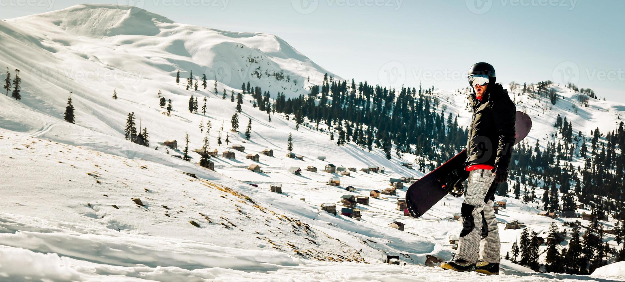 homem de snowboarder de vista lateral usa terno preto óculos máscara chapéu jaqueta acolchoada de esqui fazer gesto de vencedor comemorar isolado no topo. fundo inverno esporte radical passatempo viagem de fim de semana relaxar foto