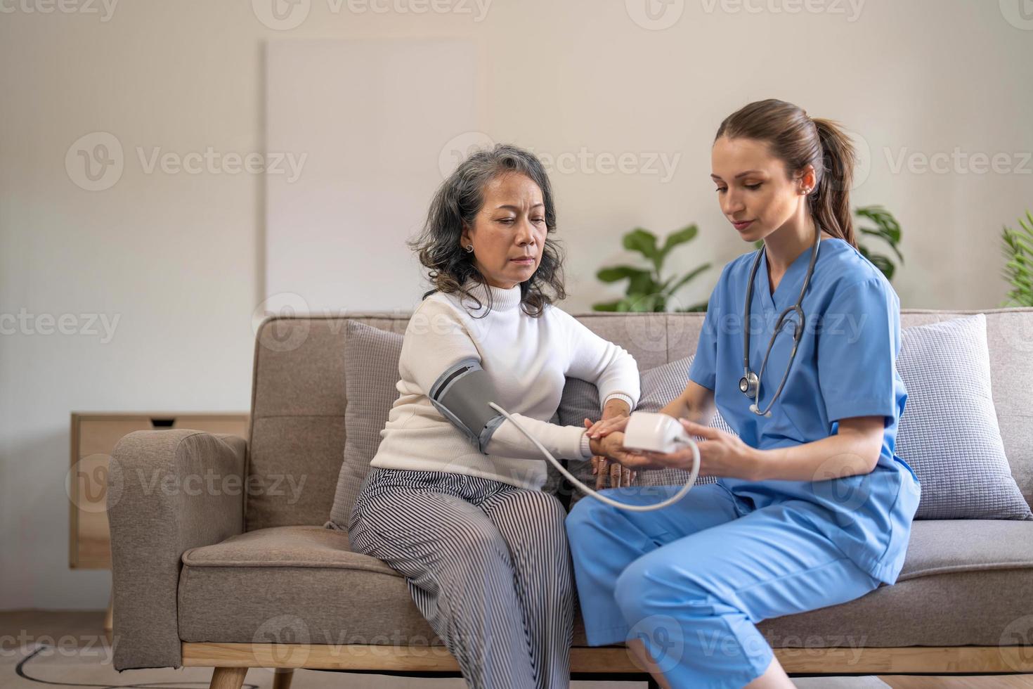 mulher sênior feliz tendo sua pressão arterial medida em um lar de idosos por seu cuidador. enfermeira feliz medindo a pressão arterial de uma mulher sênior na sala de estar foto