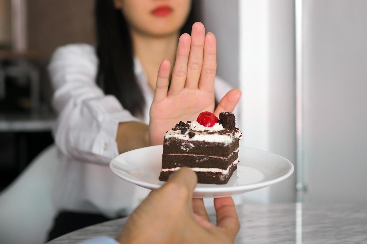 uma das moças do posto de saúde usou a mão para empurrar um prato de bolo de chocolate. recusar-se a comer alimentos que contenham gordura trans. foto