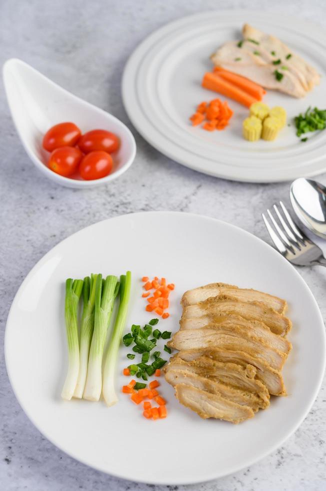 peito de frango cozido no vapor em um prato branco com cebolinhas e cenouras foto