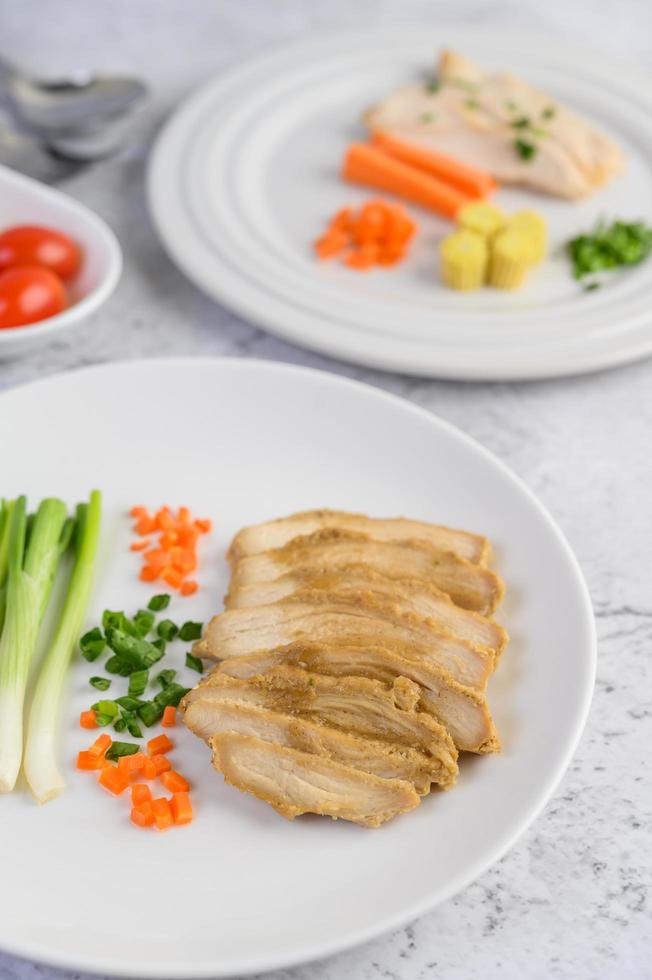 peito de frango cozido no vapor em um prato branco com cebolinhas e cenouras foto