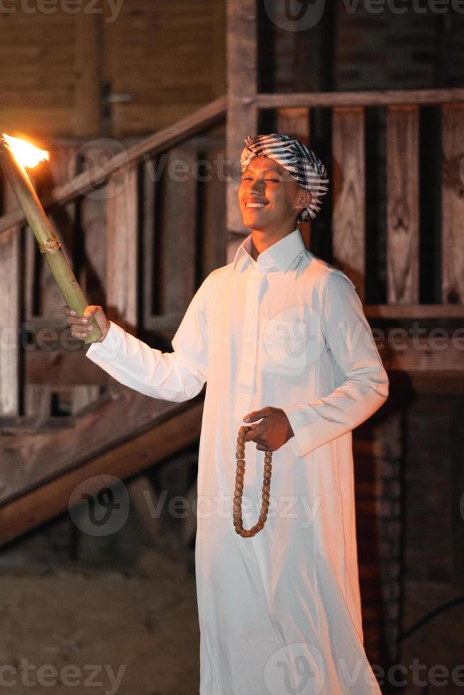 um homem islâmico vestindo um vestido muçulmano na noite escura com a iluminação da tocha de fogo foto