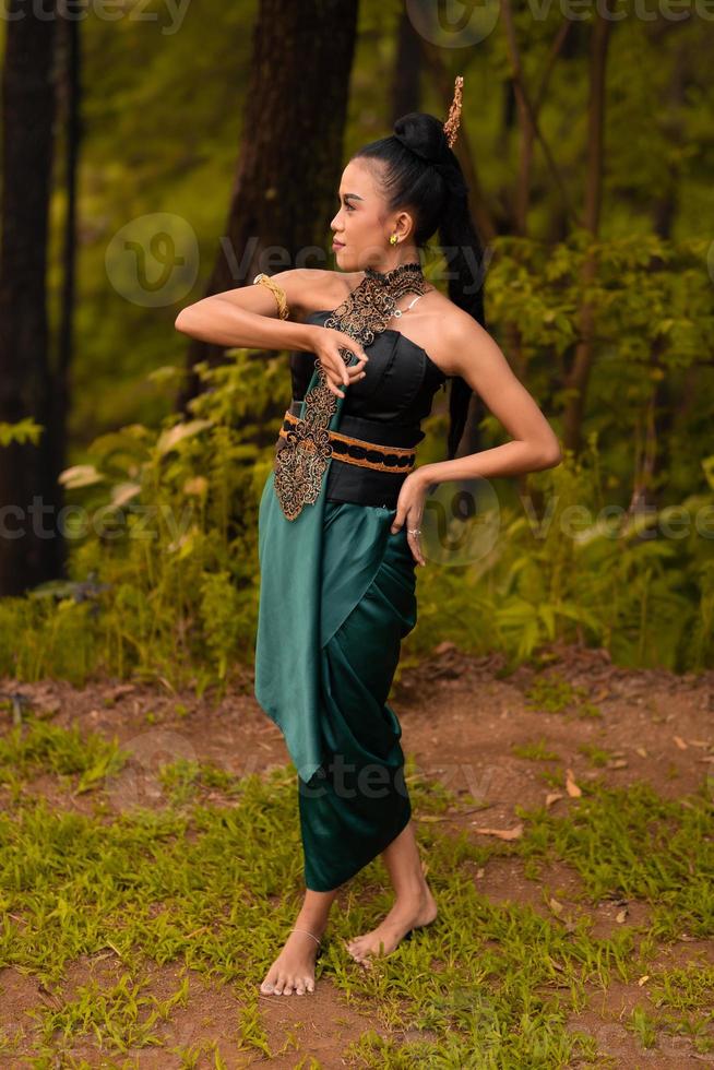 belas dançarinas indonésias com trajes tradicionais verdes e cabelo preto amarrado posando dentro da floresta foto