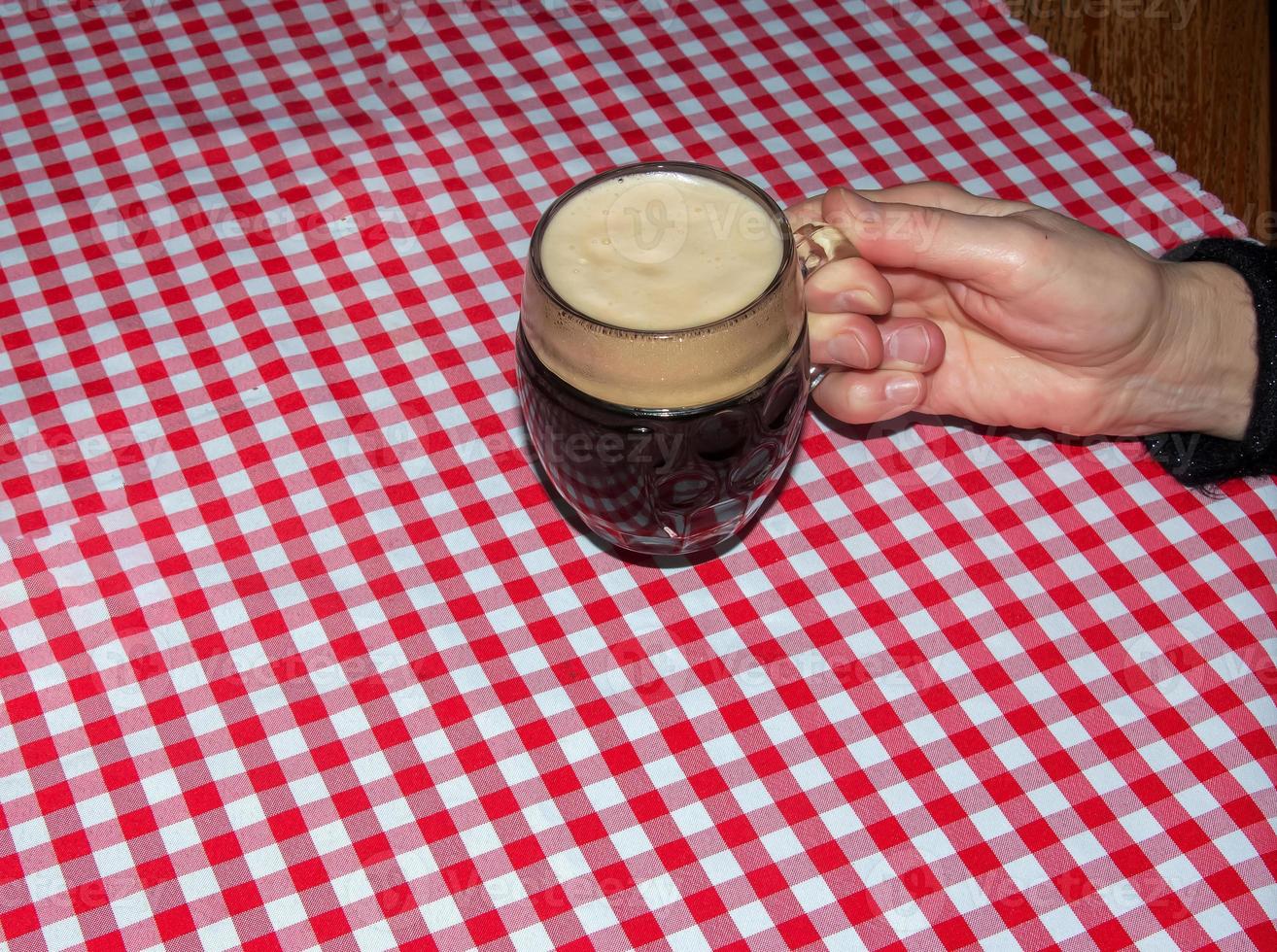 uma caneca de cerveja em uma mesa coberta com uma toalha xadrez vermelha. foto