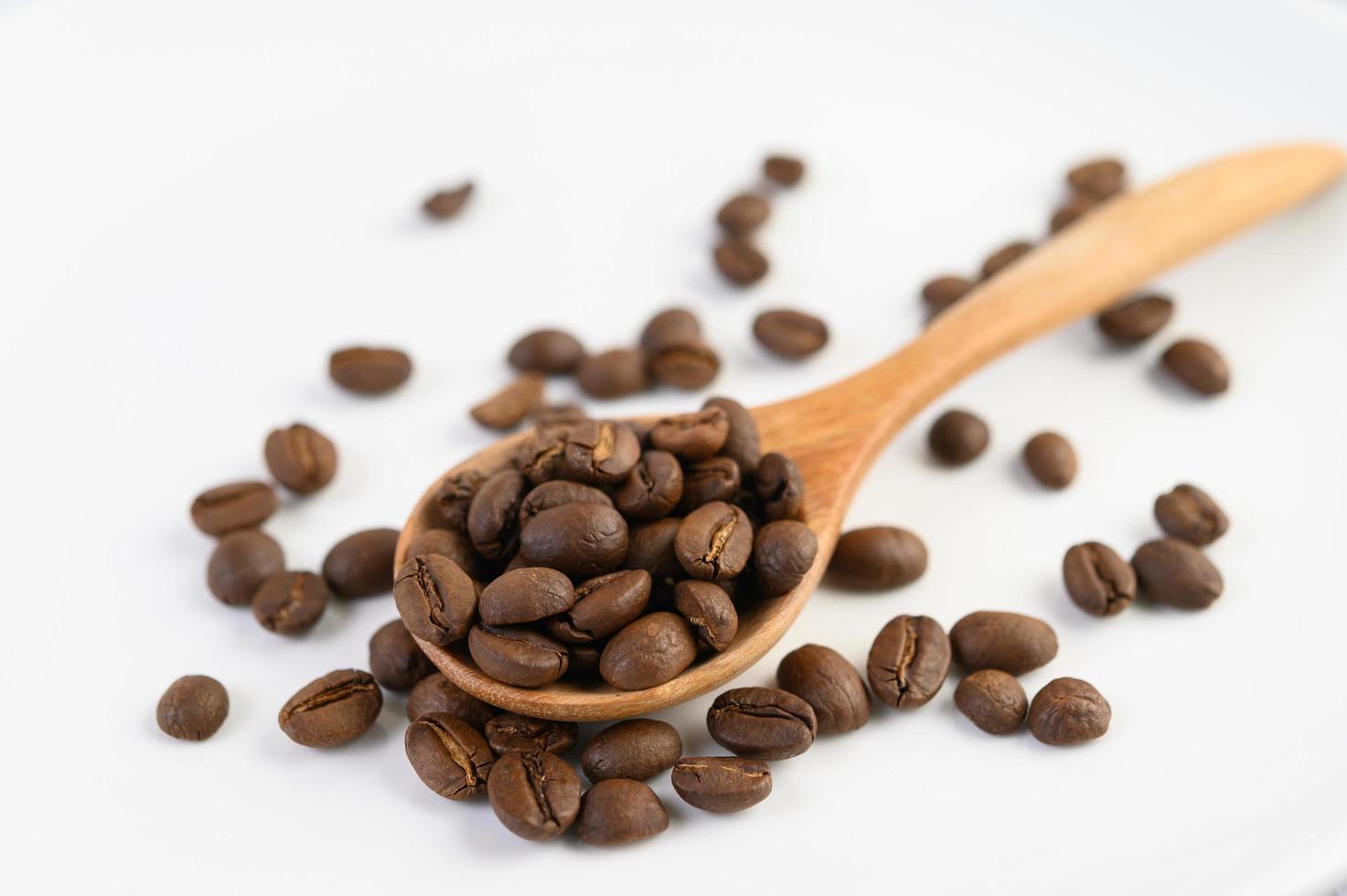 grãos de café em uma colher de pau sobre uma mesa de madeira branca foto