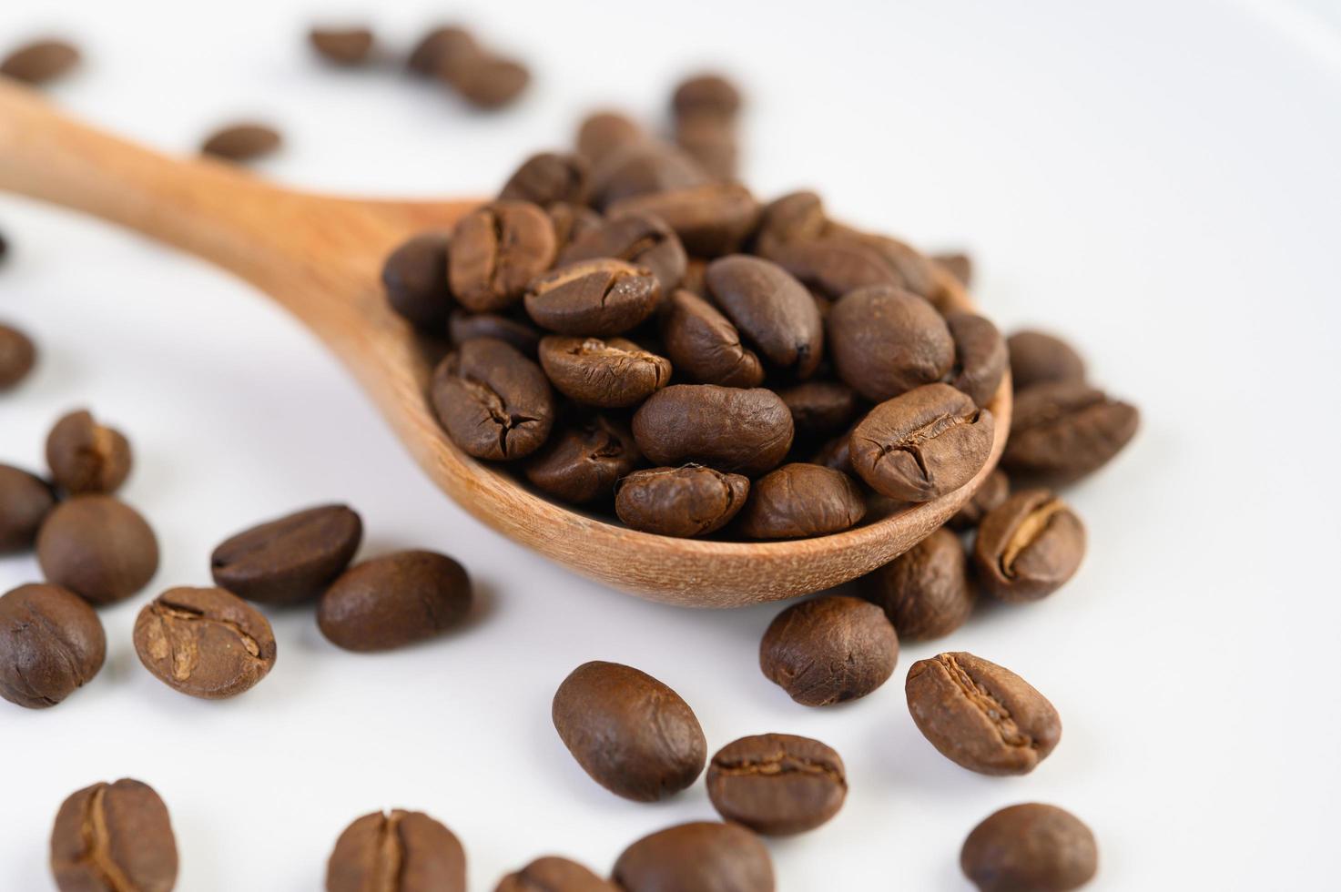 grãos de café em uma colher de pau sobre uma mesa de madeira branca foto