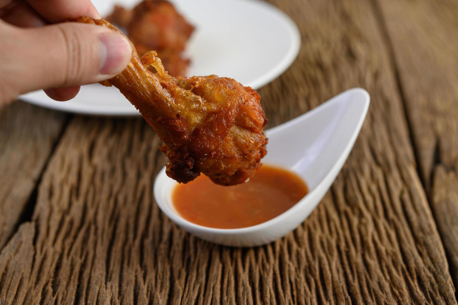 mão segurando um pedaço de frango frito com molho foto