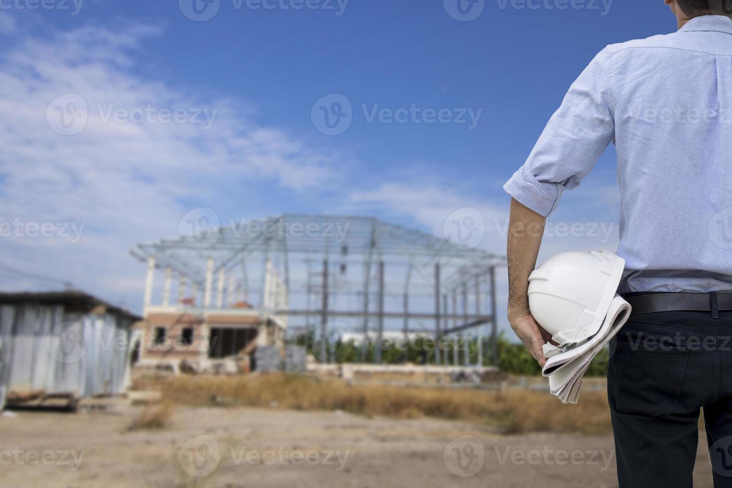 engenheiro segurando um capacete branco enquanto olha para o canteiro de obras foto