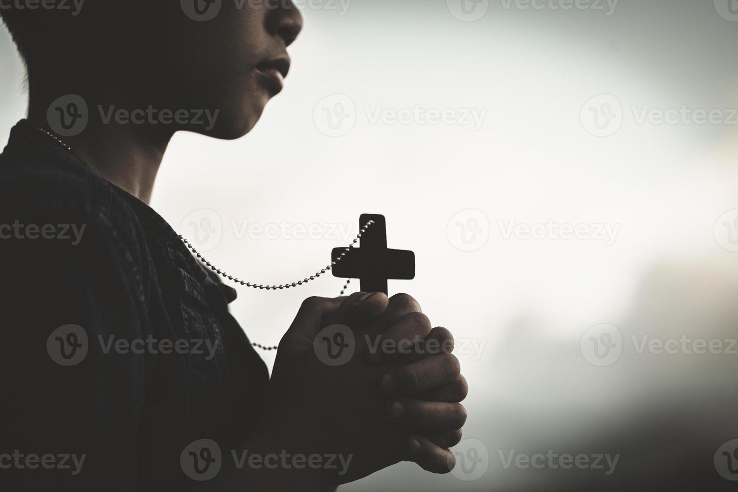 mãos de menino segurando uma cruz sagrada e orando a deus, criança orando pela religião de deus. foto