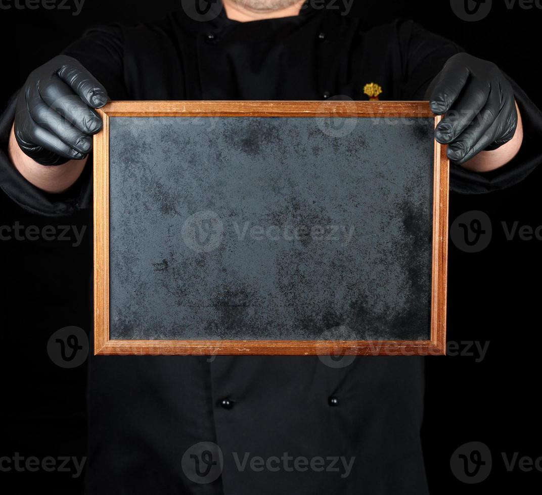 chef de uniforme preto e luvas de látex pretas segura uma moldura de madeira vazia foto