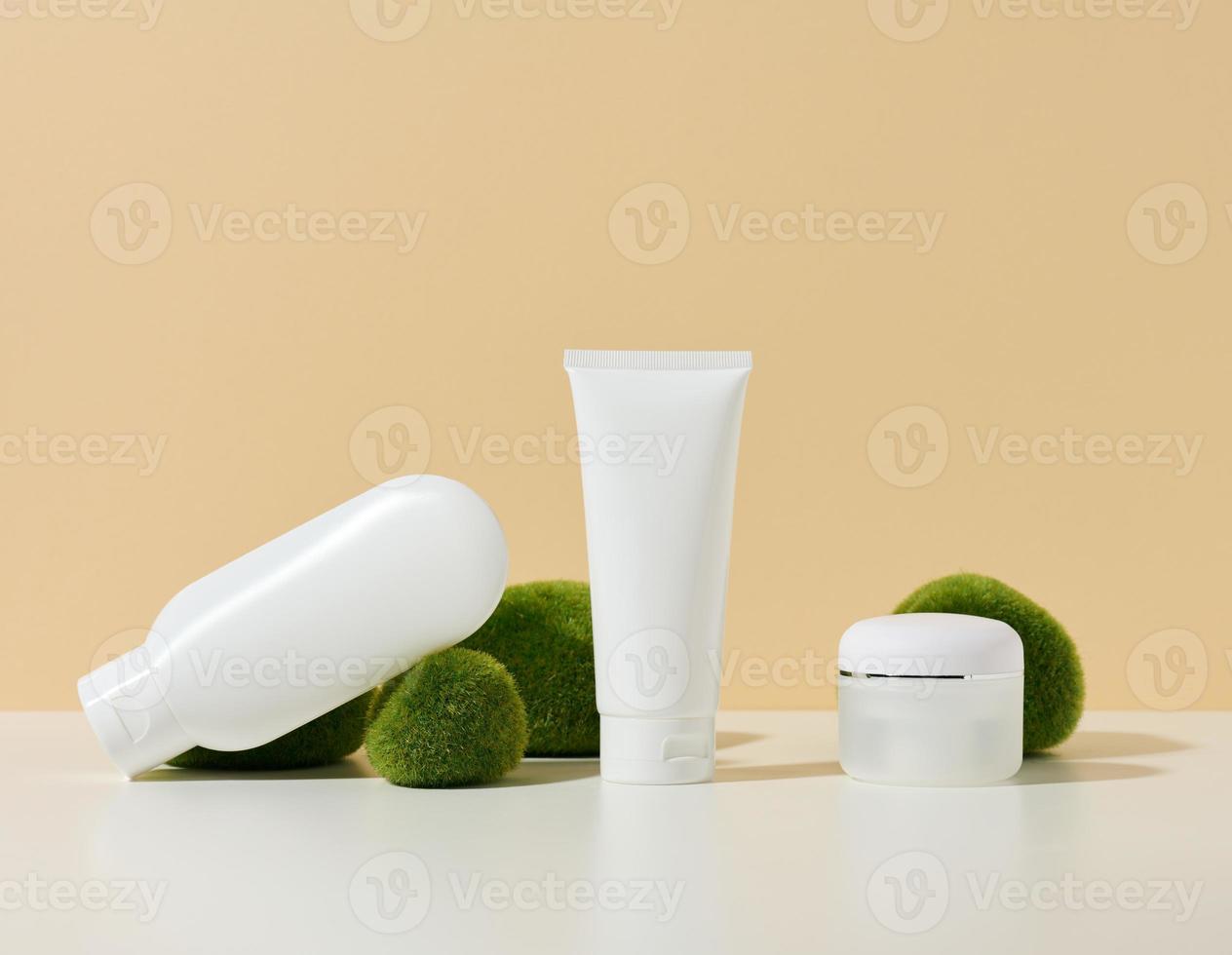 tubo de plástico branco vazio, frasco com um triturador perto de pedras com musgo em um fundo bege. produtos cosméticos para gel de marca, creme, loção, xampu. brincar foto