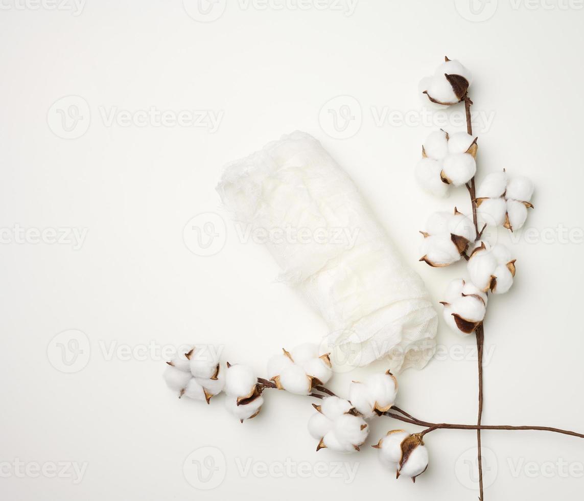 pedaço de gaze branca e um raminho com flores brancas de algodão em cima da mesa foto