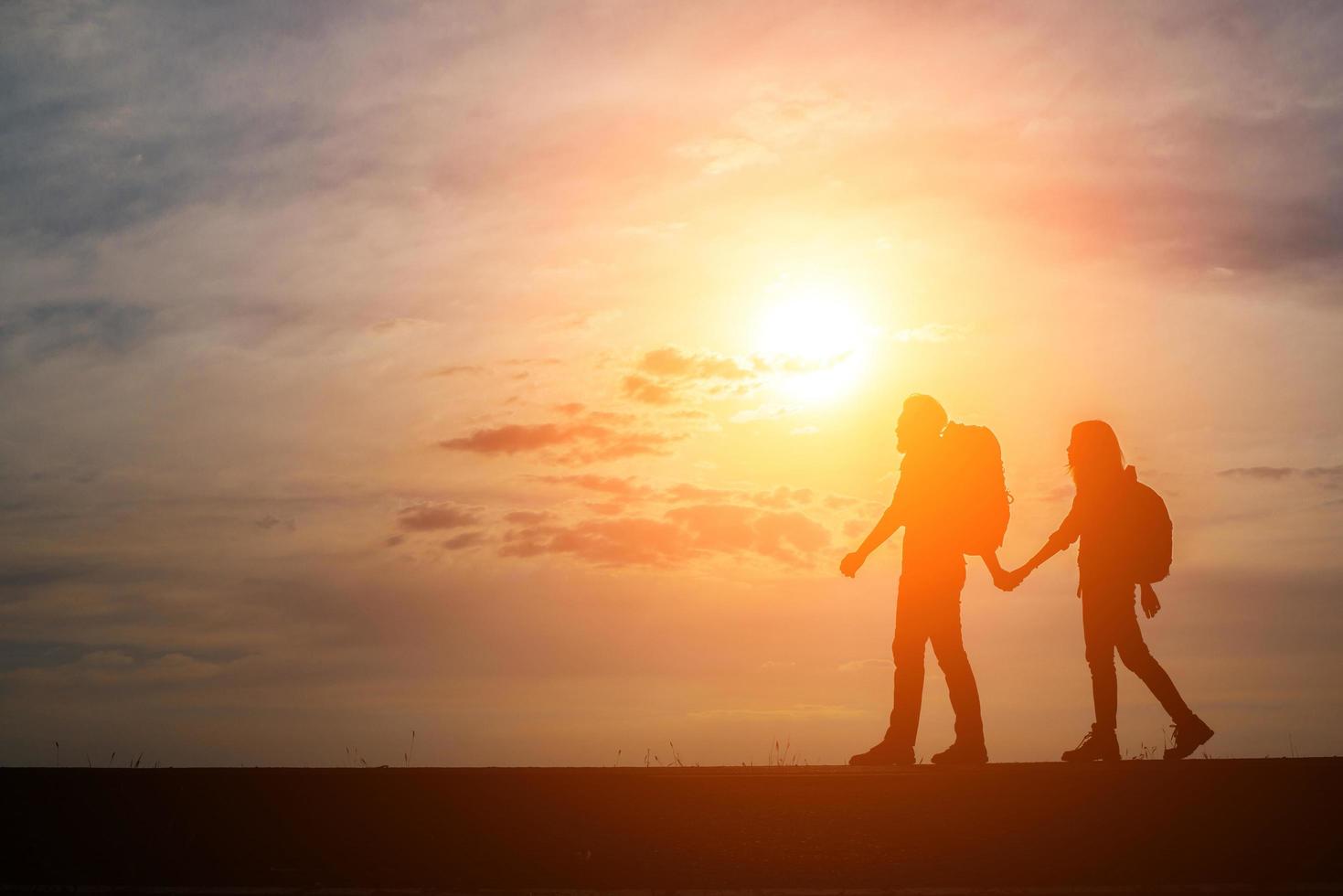 silhuetas de dois caminhantes com mochilas apreciando o pôr do sol foto