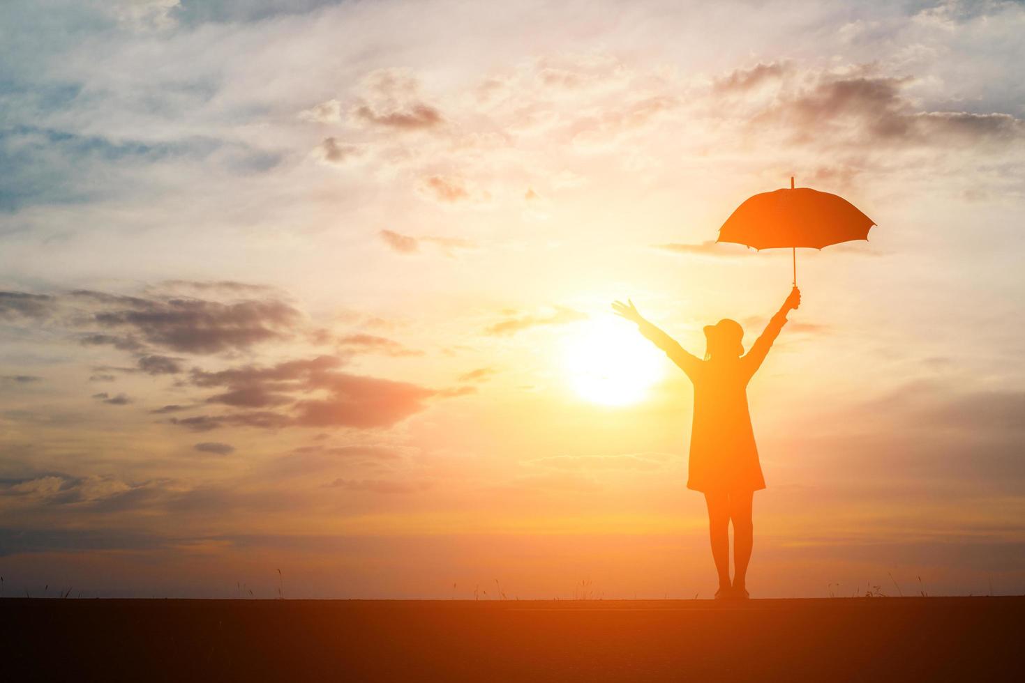 silhueta de uma mulher segurando um guarda-chuva na praia e no pôr do sol foto