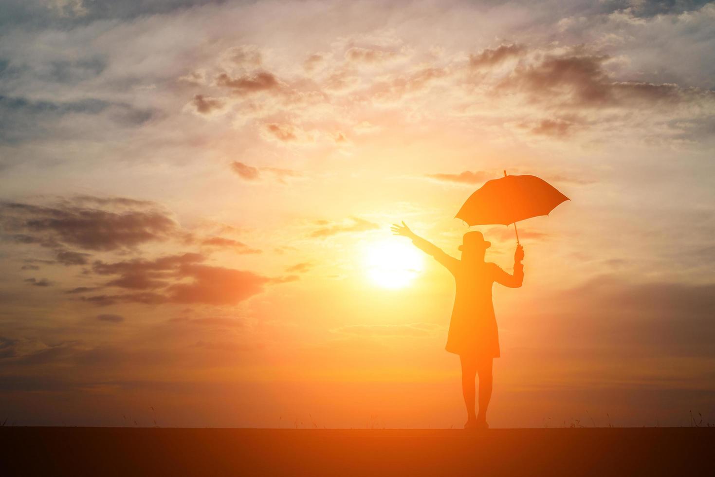 silhueta de uma mulher segurando um guarda-chuva na praia e no pôr do sol foto