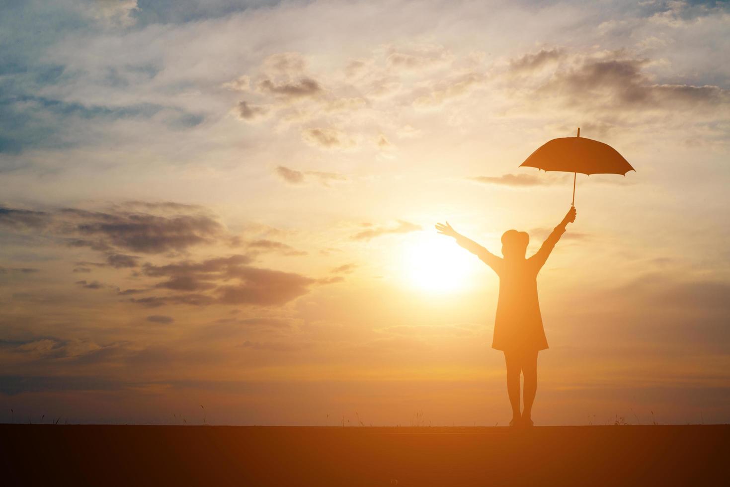 silhueta de uma mulher segurando um guarda-chuva na praia e no pôr do sol foto