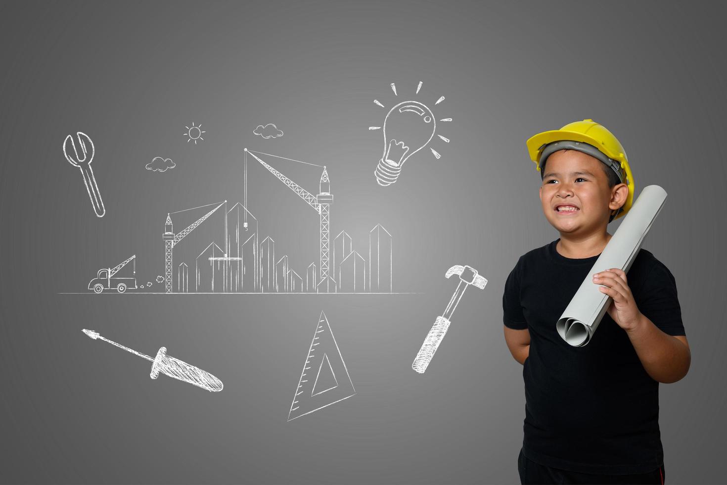 menino usando um chapéu amarelo de engenheiro e idéias de planos de casa no quadro-negro foto