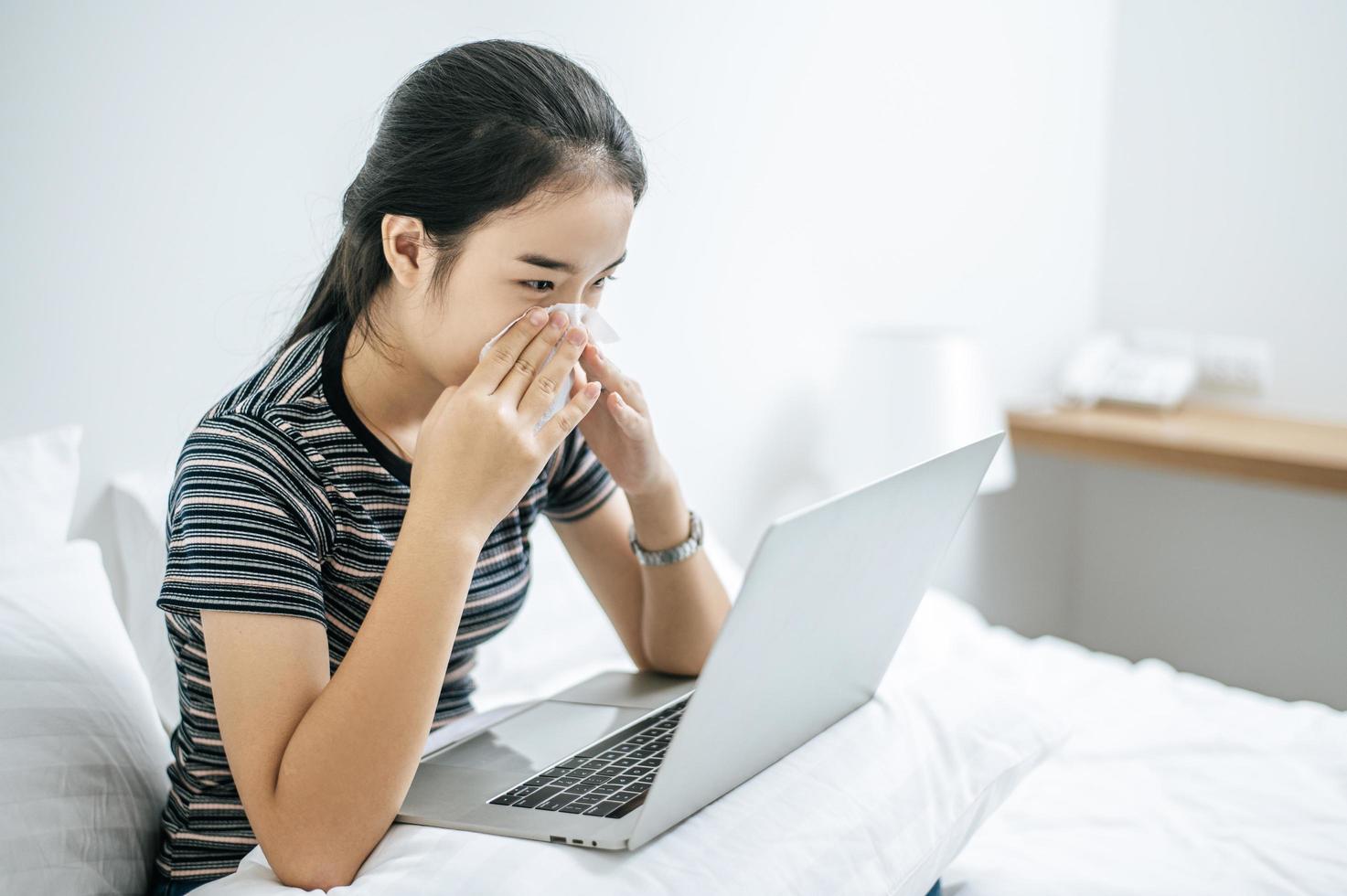 mulher brincando no laptop segurando um lenço de papel para limpar o nariz foto