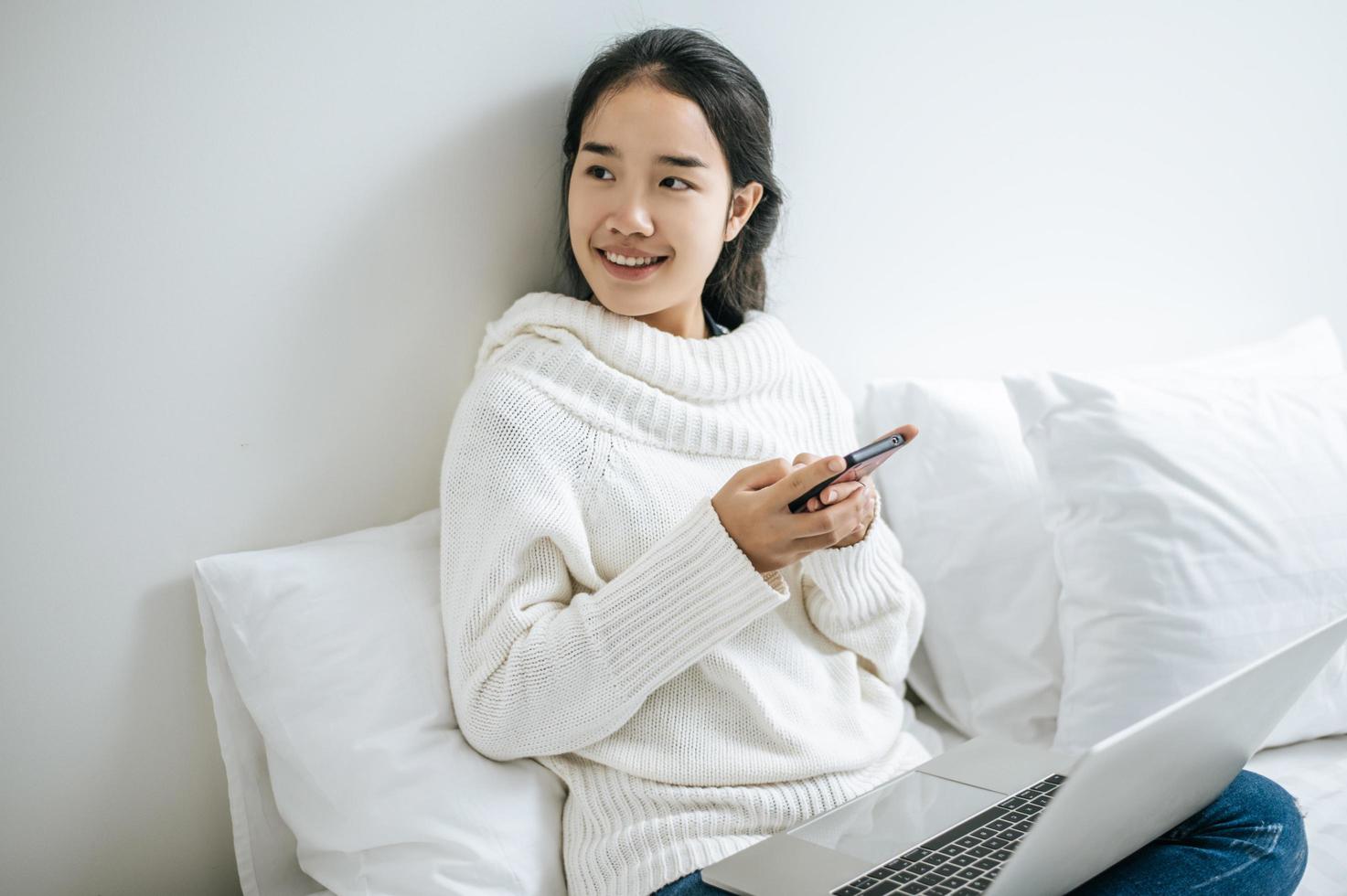 uma mulher vestindo uma camisa branca brincando em um smartphone em sua cama foto