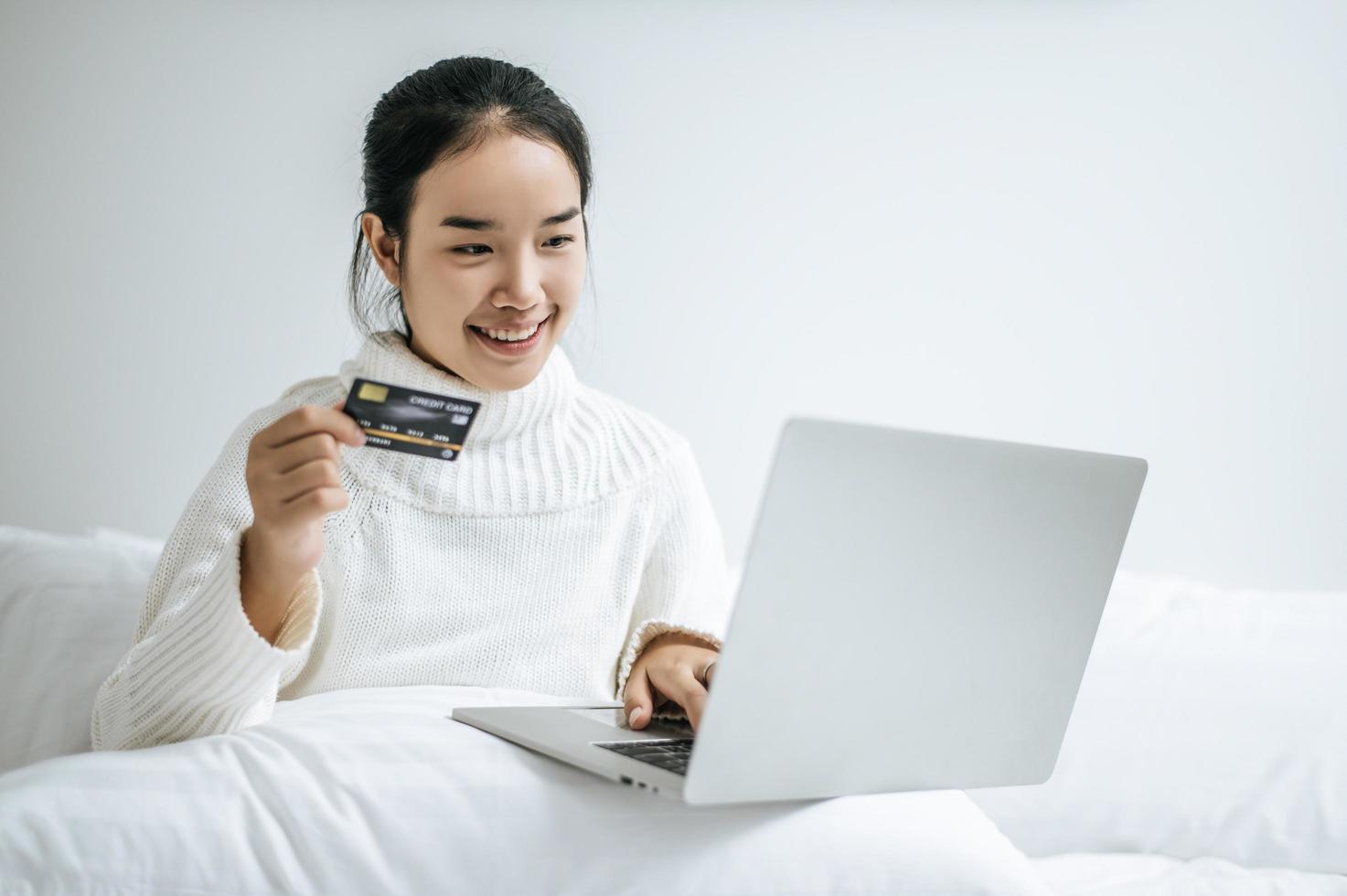 jovem fazendo compras no laptop e segurando um cartão de crédito foto