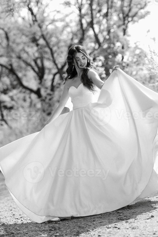 uma jovem noiva em um vestido branco está girando em um caminho foto