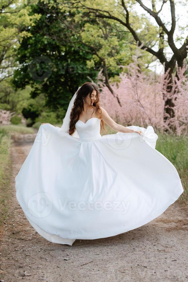 uma jovem noiva em um vestido branco está girando em um caminho foto