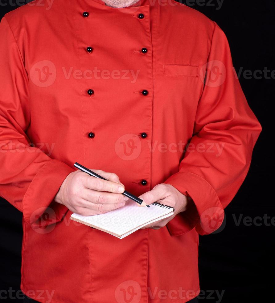 chef de uniforme vermelho segurando um caderno em branco e um lápis de madeira preto foto