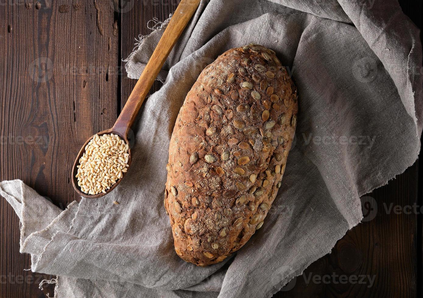 pão oval cozido feito de farinha de centeio com sementes de abóbora em um guardanapo de linho cinza foto