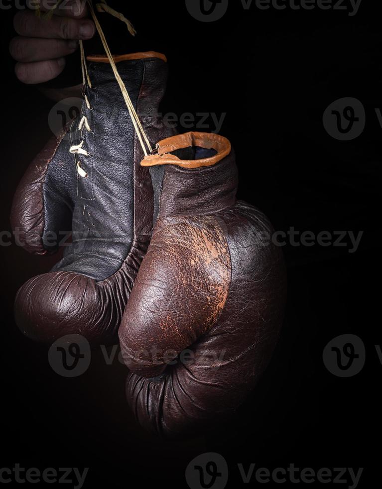 a mão segura um par de luvas de boxe marrons muito velhas foto