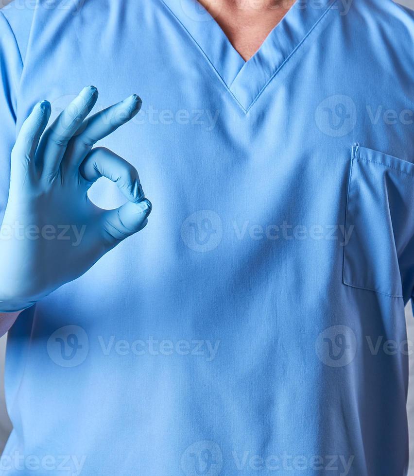 médico de uniforme azul e luvas estéreis de látex mostra um símbolo de aprovação foto