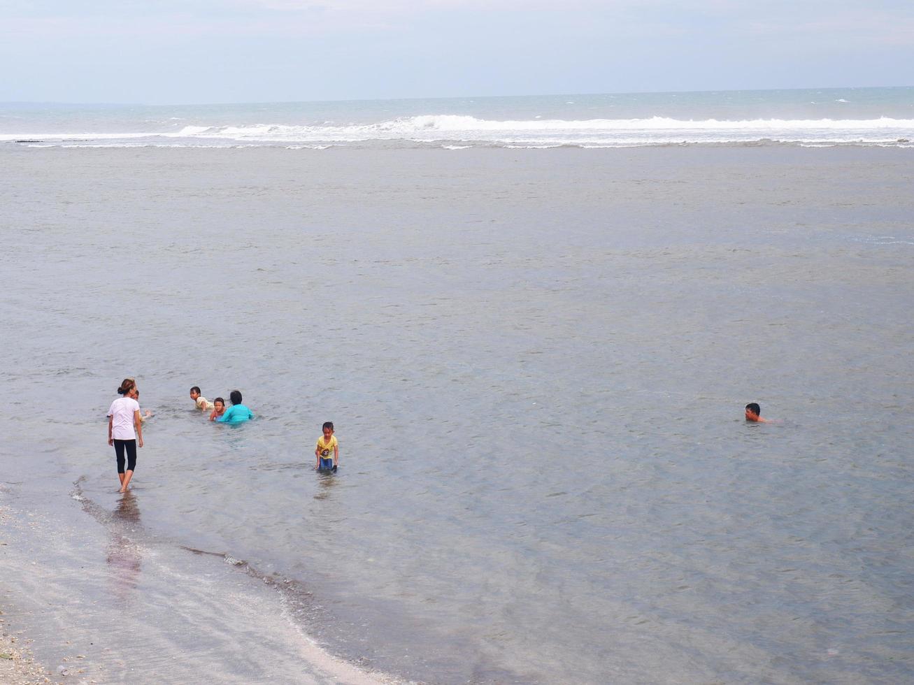 garut, indonésia-12 de dezembro de 2022 pessoas que estão brincando e nadando em uma bela praia tropical com céu azul e fundo de textura abstrata de nuvens brancas. área de praia foto