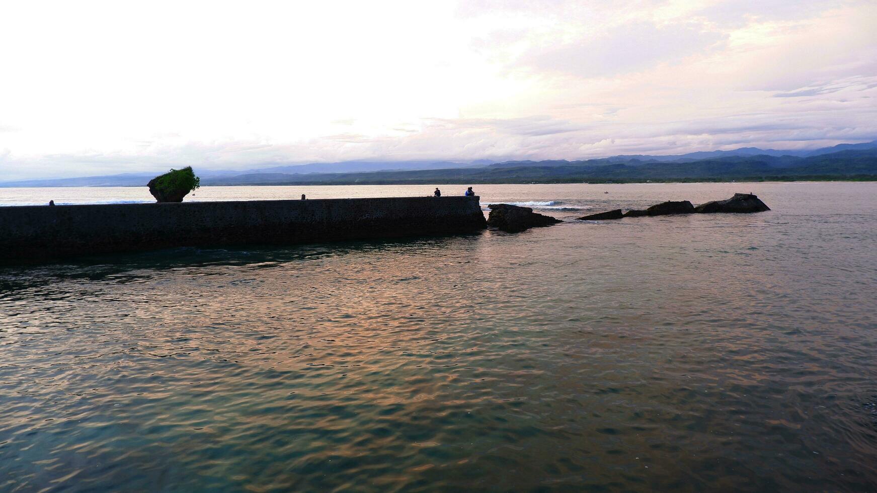 vista para o mar à tarde e paredão, praia e coral, fundo do pôr do sol na praia de santolo indonésia foto