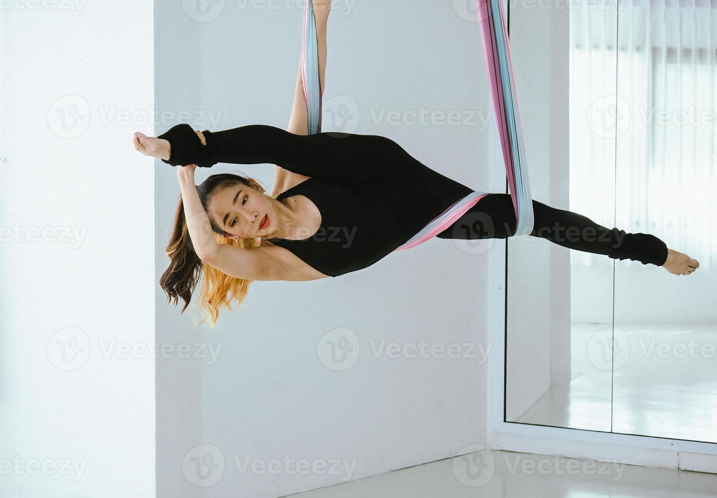 jovem bela dançarina asiática vestida de preto realizando dança aérea com tecidos multicoloridos no estúdio. foto