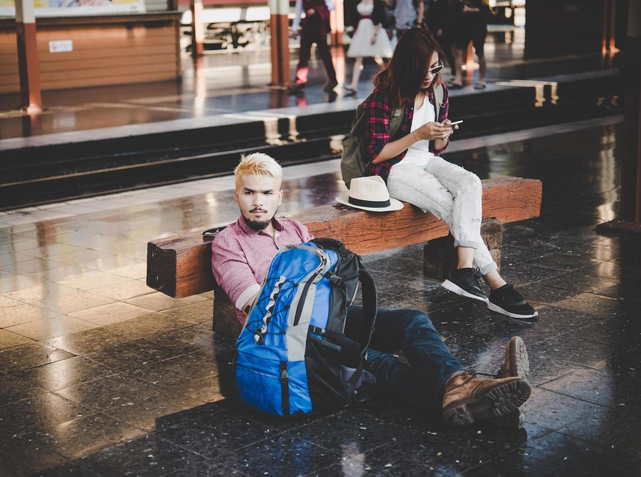 casal jovem hippie sentado em um banco de madeira na estação de trem foto