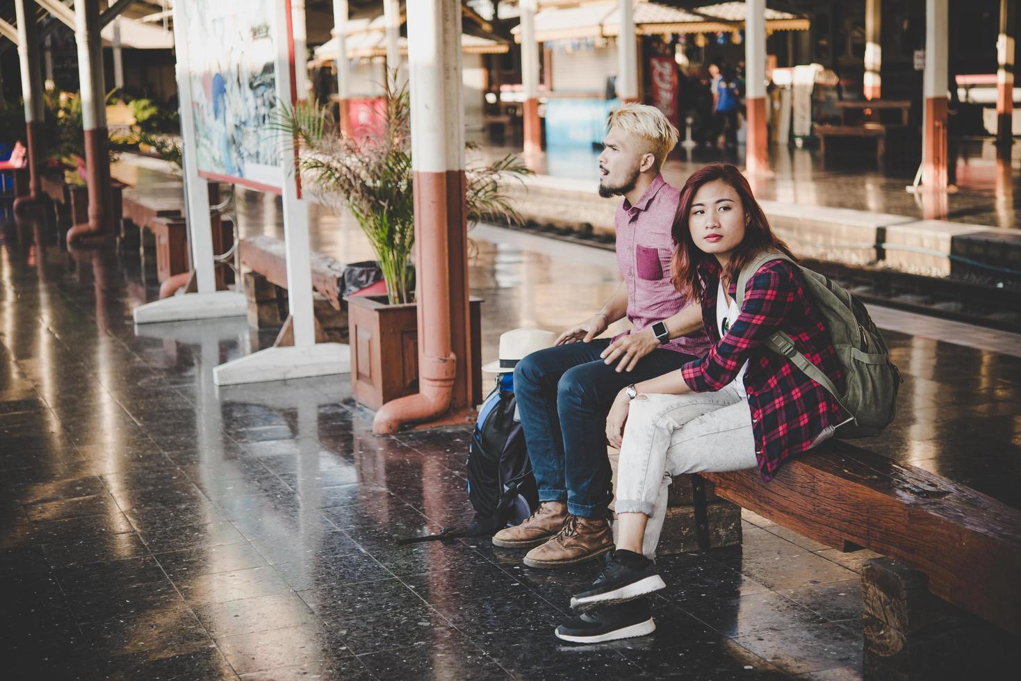 casal jovem hippie sentado em um banco de madeira na estação de trem foto