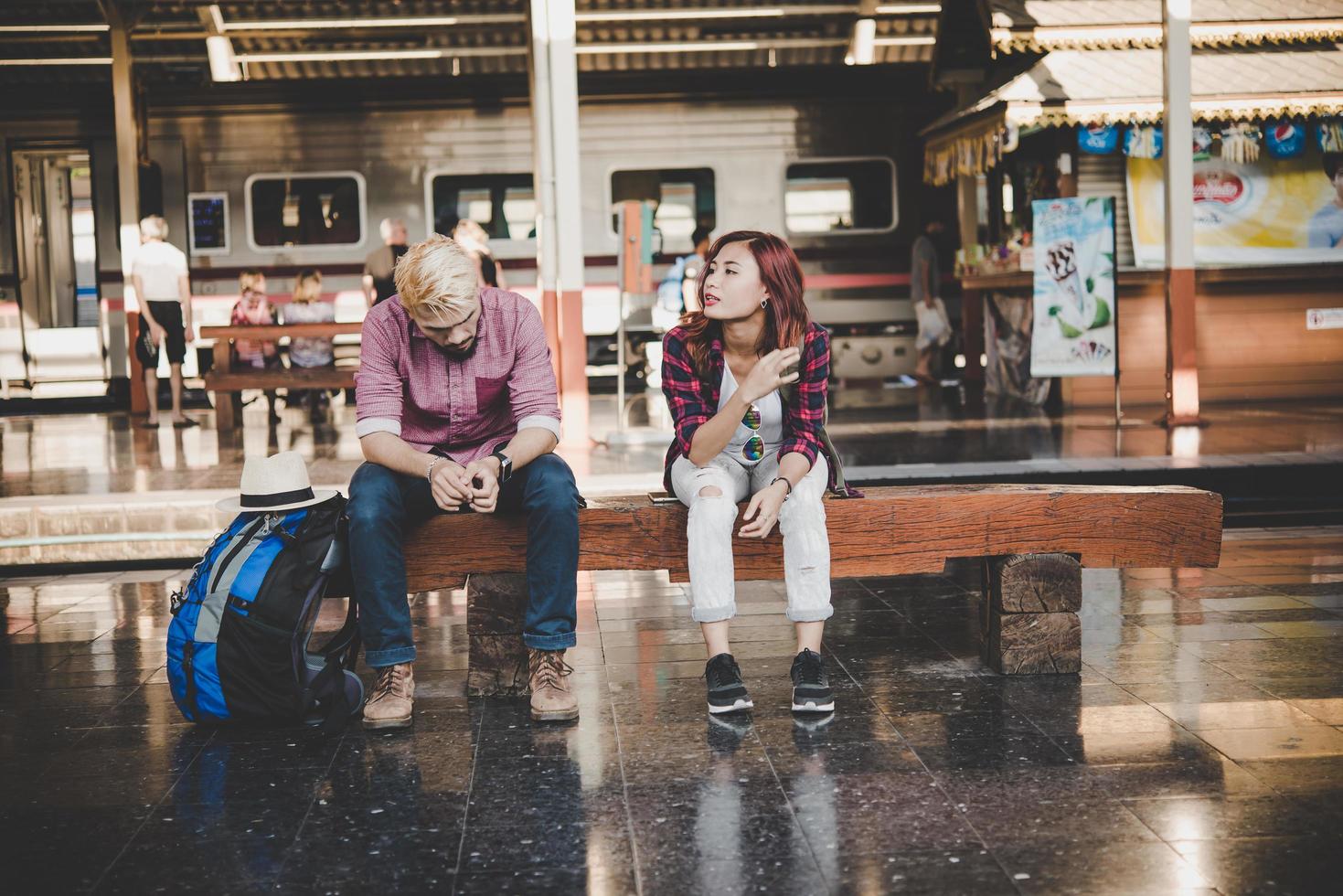 casal jovem hippie sentado em um banco de madeira na estação de trem foto