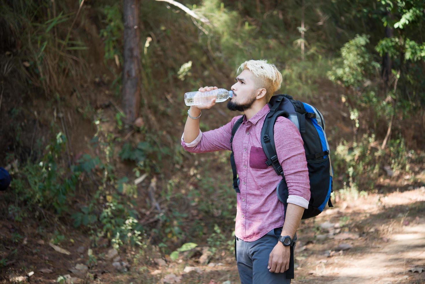 feliz hipster homem turista com mochila caminhando na floresta foto