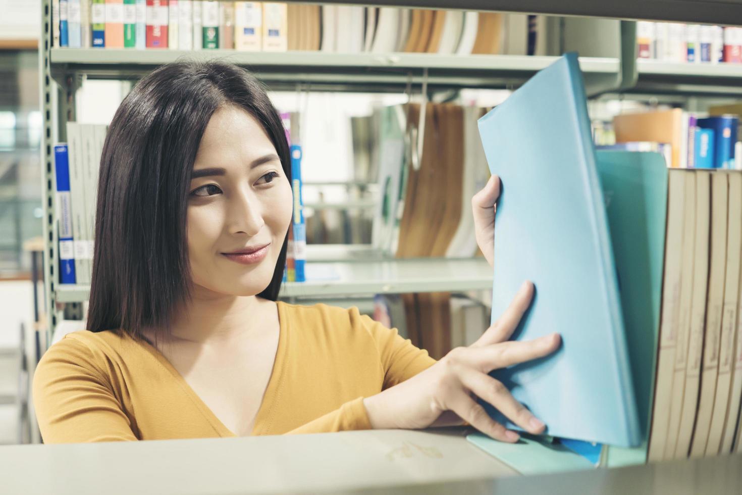 jovem estudante asiática na biblioteca lendo um livro foto