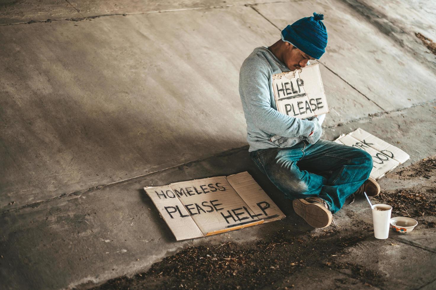 mendigo sentado sob um viaduto com placas de ajuda foto