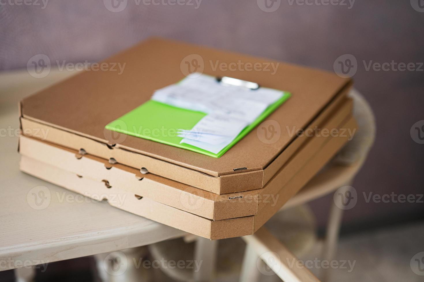 caixas de pizza de papelão com prancheta de entrega na cozinha na mesa. foto