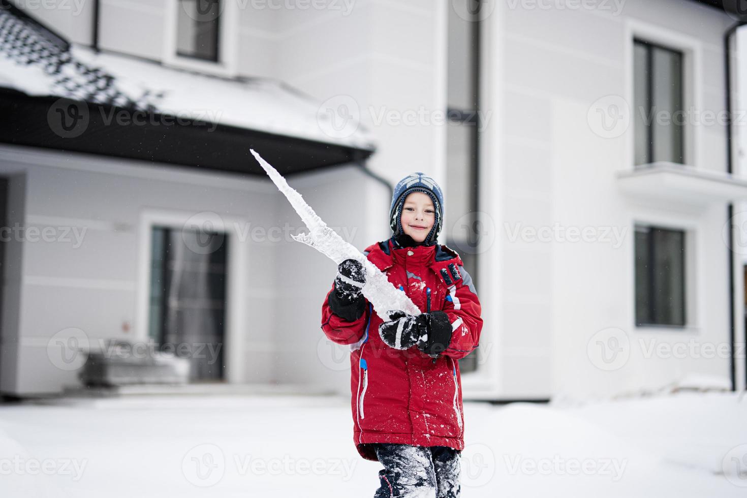 menino com grande sincelo de gelo no inverno contra a casa. foto